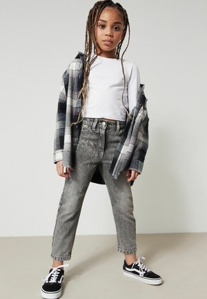 Grå rutiga flanelljacka över en vit långärmad tröja, kombinerad med slitna grå jeans och svarta Vans-sneakers. Flätat hår.