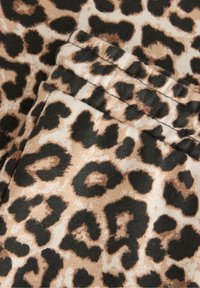 Luipaardprint stof met grote zwarte vlekken op een beige achtergrond, met een zachte textuur en gelaagde stoffen plooien.