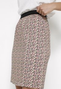 Falda de longitud hasta la rodilla con estampado floral en tela ligera. Presenta una cinturilla elástica negra. Los colores incluyen rosa, verde y blanco.