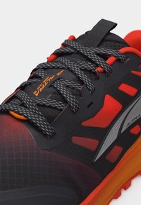 Κοντινό πλάνο μαύρου και κόκκινου αθλητικού παπουτσιού με σχέδιο στα μαύρα κορδόνια, πορτοκαλί λεπτομέρειες και τη σήμανση "ALTRA" στη γλώσσα και στην πλευρά.