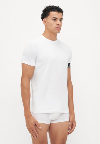 Weißes Baumwoll-T-Shirt mit kurzen Ärmeln und rundem Halsausschnitt. Verfügt über einen schwarzen grafischen Akzent am linken Ärmel. Glatte Textur.