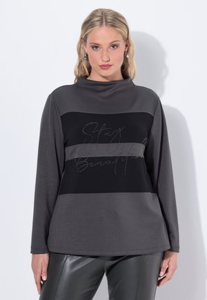 Haut à manches longues en gris foncé et noir, avec un col montant et des rayures horizontales, orné de texte en sequins disant "Restez Belle" sur la poitrine.