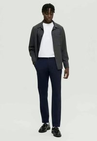 Σκοτεινό γκρι πουκάμισο πάνω από λευκό μπλουζάκι, συνδυασμένο με ναυτικό παντελόνι και μαύρα παπούτσια, με κομμένα ρούχα και μίνιμαλ σχέδιο.