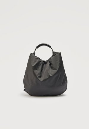 Čierna mäkká látková kabelka s zaobleným horným rúčkou, mierne pokrčená textúra, na jednoduchom svetlosivom pozadí.