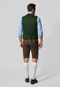 Groene gilet over een blauw geruit shirt, gecombineerd met een paarse kniebroek, witte kniesokken en bruine schoenen. Eenvoudig, traditioneel ontwerp.