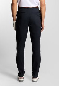 Pantalone za golf u mornarsko plavoj boji od pamuka s dva zadnja džepa, koji su upareni s smešnim pletenim remenom i belim patikama s crvenim i sivim akcentima.