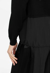 Mustvalge kihiline topp , mis sisaldab kudumist �ülemises osas ja kergest tekstuuriga alumises osas. Vöökoht on elastse nööriga reguleeritav.