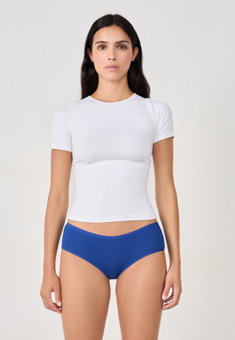 Top bianco a maniche corte con un design aderente, abbinato a slip blu a vita bassa con fascia morbida.