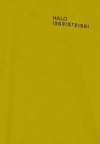 Gul bomullströja med en texturerad svart tryck med "HALO 196819721981" placerad i det övre vänstra hörnet.