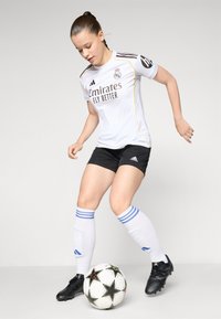 Biely futbalový dres s čiernymi a zlatými akcentmi, čierne šortky, bielo pruhované modré ponožky, čierne kopačky a futbalová lopta so vzorom hviezd.