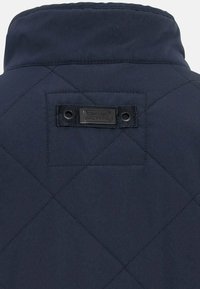 Navy gesteppte Jacke auf der Rückseite mit hohem Kragen, Stoffetikett mit Markennamen und horizontalen Nähten für Textur.