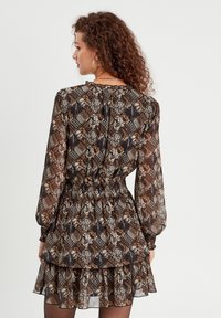 Robe noire et brune à motifs avec des designs floraux et géométriques, manches longues, ourlet volanté et taille smockée.