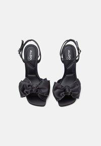 Mustad avatud varvastega sandaalid, millel on pahkluupannal töötavad rihmad, esirihmade kaunistamiseks on suurte kangast paeltega, mis on ehtitud helmestega.