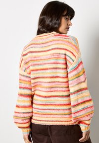 Wielokolorowy sweter w paski, wykonany z miękkiej dzianiny, z dużymi rękawami i okrągłym dekoltem. Kolory to różowy, żółty, czerwony i niebieskie akcenty.