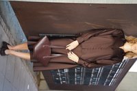 Blouse marron en soie avec des détails de boutons, portée avec une jupe assortie et des chaussures foncées. Présente un sac à main en cuir bourgogne avec des doubles poignées.