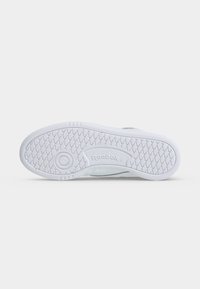 Biela podrážka topánky s diamantovým vzorom dezénu a kruhovým úchopom, s logom Reebok vyrazeným v strede.