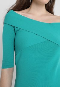 Türkisfarbener Rippstrick-Top mit einem schulterfreien Design, das kontrastierende, diagonale Schnittlinien und Dreiviertelärmel aufweist.