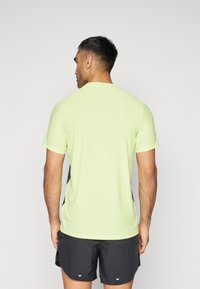 Camiseta deportiva de manga corta verde neón con acentos laterales negros, escote redondo y tejido texturizado, combinada con pantalones cortos deportivos negros.