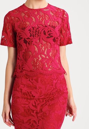 Vrouw draagt een rood kanten top met korte mouwen en een bijpassende hoge taille kanten rok met bloemmotieven.