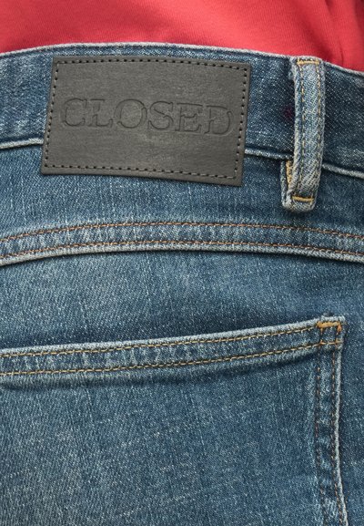 Jean en denim avec un patch en cuir noir portant l'inscription "CLOSED" à la taille. Caractérisé par des coutures orange et un design traditionnel à cinq poches.