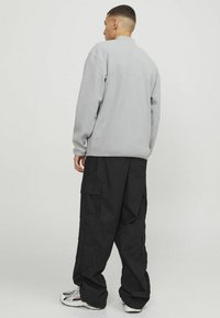 Grå fleecepullover med høj krave, parret med sorte cargo-bukser med flere sidelommer og hvide sportsko.