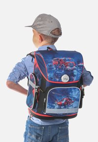 Zaino con un design blu e rosso caratterizzato da grafiche di camion dei pompieri e elicotteri, realizzato in materiale resistente, con una zip prominente e dettagli a quadri.