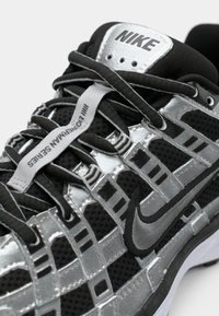 Primo piano di una sneaker Nike nera e argento con lacci neri, il logo swoosh Nike e il testo "EDGEMAN SERIES" su un'etichetta bianca della lingua.