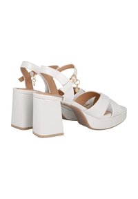 Sandalias de plataforma blancas con tiras cruzadas anchas y tacón cuadrado. Presentan un material sintético suave y herrajes en tono dorado.