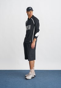 Svart langermet treningstopp med hvite stripesider og "NIKE AIR"-tekst, kombinert med svarte shorts og grå treningssko.