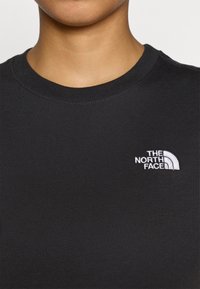 Μαύρο T-shirt με στρογγυλή λαιμόκοψη, κατασκευασμένο από λεία ύφανση, με λευκό κεντητό λογότυπο "The North Face" στο αριστερό μέρος του στήθους.