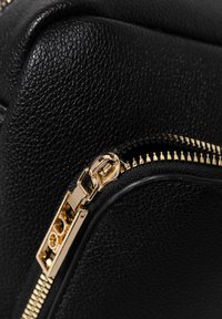 Angolo di una borsa in pelle nera con texture, dotata di una cerniera dorata. La cerniera è parzialmente aperta, mettendo in mostra denti lucidi e un dettagliato tira cerniera.