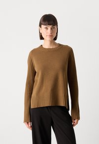 Bruin gebreid sweater met een geribbelde textuur, ronde halslijn en zijsplitten. Lange mouwen hebben geribbelde manchetten en worden gecombineerd met zwarte broeken.