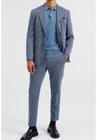 Mörkblå strukturerad kostym för män med skräddarsydd passform, bestående av en blazermedel och matchande byxor. Kompletteras av en blå pikétr öja och läderskor.