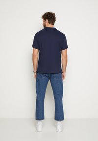 Marineblaues Polohemd mit kurzen Ärmeln, kombiniert mit hellblauen, geraden Jeans. Weiße Sneakers vervollständigen das Outfit.