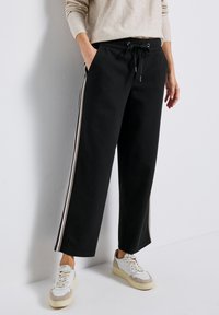 Svarta vida sweatpants med resårmidja, dragsko och kontrasterande sidostycken i krämfärg. Kombinerat med ljusa sneakers.