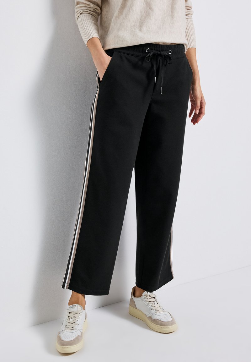 Svarta vida sweatpants med resårmidja, dragsko och kontrasterande sidostycken i krämfärg. Kombinerat med ljusa sneakers.