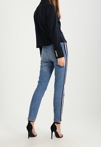 Svart långärmad topp med knappp_detajer, i kombination med ljusblå upp-och-ned-byxor med sidostripes och svarta högklackade skor.