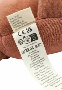 Soft, pink cotton plush with a textured surface. Care label displays washing instructions and material composition. Round shape with a stitched tag.