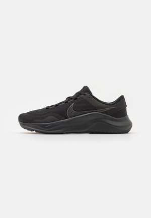 Zapatilla de correr Nike negra de corte bajo con parte superior de malla, cuello acolchado, cordones y suela curva sobre un fondo blanco liso.