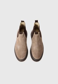 Et par beige ruskinds slip-on ankelstøvler med mørkebrune elastiske sidepaneler og trækstænger, set ovenfra på en hvid baggrund.