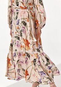 Blomster maxi kjole i beige stof med lilla, orange og grønne mønstre; har en lagdelt nederdel, lange ærmer og et bånd i taljen.