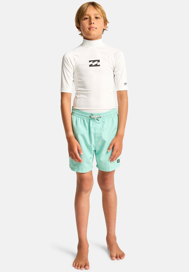 Rash guard à manches longues blanc avec un logo noir, assorti à un short de bain vert menthe avec un cordon de serrage et un patch logo latéral.