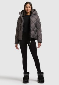 Puffjakke i mørkegrå med hætte, prydet med et diamantquiltet mønster, frontlynlås og to sidelommer. Båret med sorte leggings og støvler.