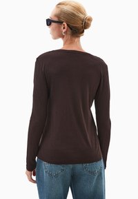 Bruine lange mouwen shirt gezien vanaf de achterkant, met een relaxte pasvorm en ronde halslijn, gecombineerd met lichtblauwe hoge taille jeans.