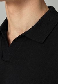 Polo noir avec un col texturé, doté d'une ouverture à demi-fermeture éclair au niveau du col. Le tissu semble doux et lisse avec une coupe ajustée.