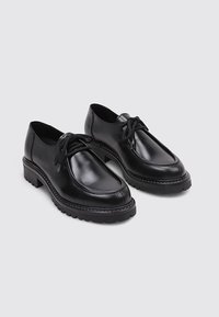 Zapatos de cuero negro con puntera redonda, suela de goma gruesa y cordones. Textura suave y acentos sutilmente cosidos alrededor de los bordes.