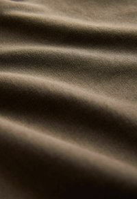 Textilstoff in einem gedeckten Braunton, mit sanften, strukturierten Falten und subtilem Glanz, der auf eine glatte Oberfläche und leichte Qualität hinweist.