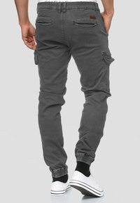 Pantaloni cargo grigi in misto cotone, con tasche laterali e polsini elastici, abbinati a sneakers bianche e calzini neri.