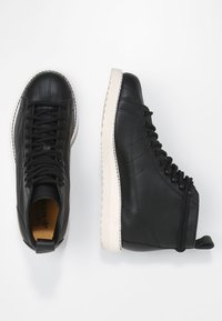 Black high-top sneakers made of leather with a textured surface, white rubber sole, and lace-up design featuring a pull tab at the heel.