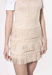 Vestido de ante beige con capas de flecos verticales y tachuelas metálicas, cuerpo ajustado y textura suave.